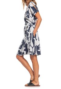 Bloemenwikkeljurk in marineblauw met witte bladmotieven; korte mouwen, tailleband en zakken, gemaakt van een lichtgewicht stof.