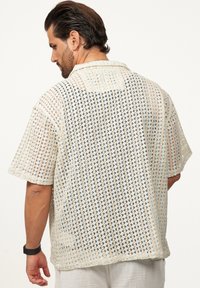 Kurzärmliges Hemd aus einem leichten, offen gestrickten Stoff mit einem geometrischen Muster in Beige- und Schwarztönen. Mit Button-Down-Kragen.