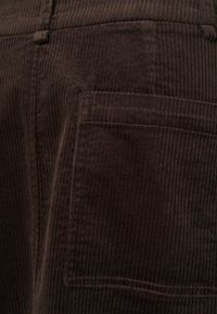 Tessuto di velluto a coste marrone che mostra una texture a coste verticali con un dettaglio della tasca sul lato. Il design presenta un aspetto morbido e peloso.