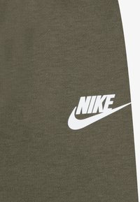 Maslinasto zeleni materijal s mekom teksturom, sa istaknutim bijelim Nike logotipom. Dizajn je jednostavan, naglašavajući funkcionalnost i identitet brenda.