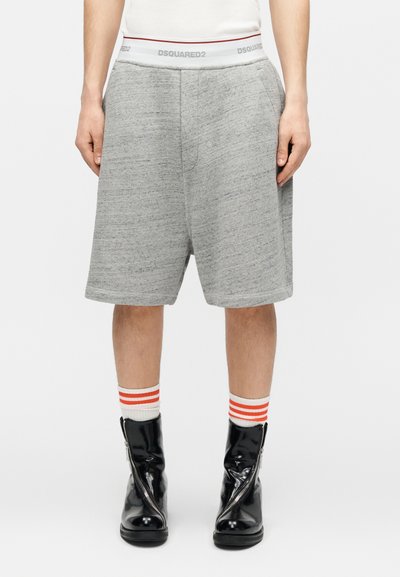 Άτομο που φοράει κοντά σορτς ανοιχτού γκρι χρώματος μέχρι τα γόνατα, λευκή ζώνη με το κείμενο "DSQUARED2", λευκές κάλτσες με πορτοκαλί ρίγες και μαύρα μποτάκια με φερμουάρ.