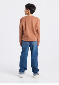 Brown long-sleeve sweatshirt paired with blue wide-leg jeans and white sneakers. Smooth texture and relaxed fit, visible stitching details.