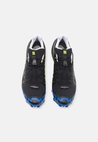 Schwarze Trailrunning-Schuhe mit strukturierten Oberflächen, blauer Laufsohle, reflektierenden Akzenten und einem Schnellverschluss-System für einen sicheren Sitz.