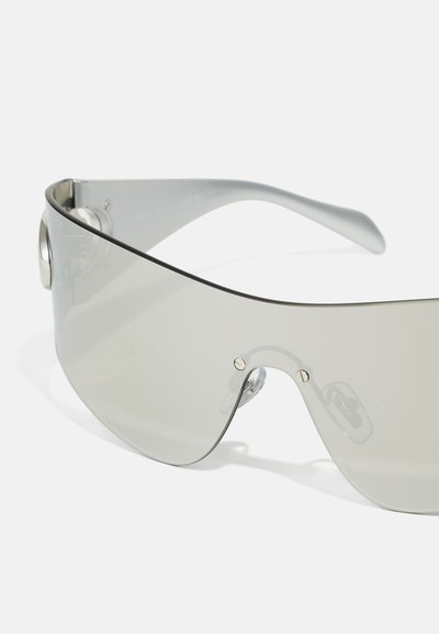Sonnenbrille mit grauem getönten Glas, geschwungenem Design und klaren Rahmenakzenten. Verfügt über metallische Elemente und verstellbare Nasenpolster für Komfort.