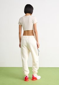 Κοντομάνικη μπεζ μπλούζα, λευκό παντελόνι φόρμας με μαύρο κορδόνι και αθλητικά παπούτσια με ροζ σόλα. Απαλή βαμβακερή ύφανση με χαλαρή εφαρμογή.