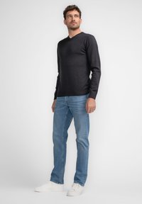 Pulover gri închis, cu decolteu în V, dintr-un material tricotat fin, asortat cu blugi albaștri deschiși și adidași albi. Design simplu, ajustat, cu accente ribbate.