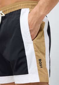 Plavkové šortky s farebnými blokmi v čiernej, bielej a hnedej farbe, s elastickým pásom a logom na boku.