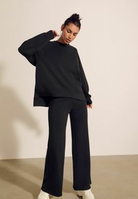 Crni oversized dukserica i odgovarajuće široke hlače od mekanog materijala. Outfit ima opušteni kroj i čiste linije, bez vidljivih uzoraka.