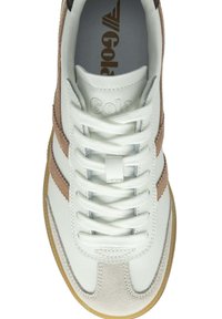 Zapatilla blanca con acentos de gamuza marrón y franjas laterales texturizadas. Presenta cordones blancos, un collar acolchado y una suela de goma.