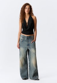 Top negro tipo halter con tejido drapeado y escote profundo, combinado con jeans de pierna ancha de ajuste holgado y deslavados en azul, con bolsillos frontales.