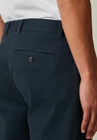 Pantalonii în nuanță închisă de navy au un material texturat, croi slim și o buzunare la spate cu nasture. Talie este plată, cu bucle pentru curea, pentru ajustarea mărimii.