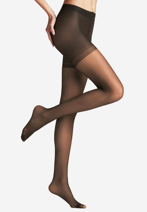 Person wearing sheer black pantyhose with one leg bent and hand resting on the hip against a plain white background.