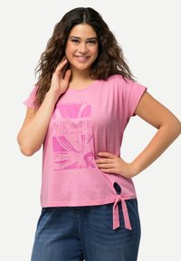 Růžové tričko s krátkým rukávem, s grafickým potiskem a uzlovým detailem na boku. Měkká, lehká tkanina s volným střihem.