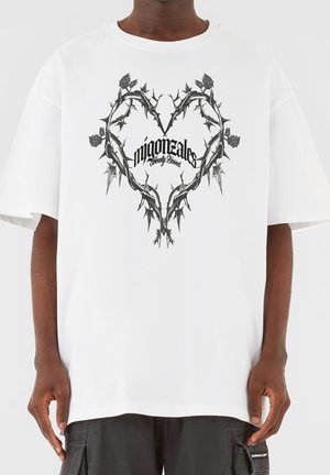 Biała, oversize'owa koszulka z czarną grafiką serca z cierniami oraz napisem „migonztales Eternally Blessed” pogrubioną czcionką. Krótkie rękawy.