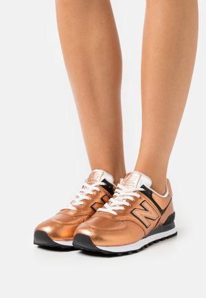 Brązowe metaliczne sneakersy z białymi sznurowadłami, z czarnym akcentem, teksturowaną powierzchnią i wyściełanym kołnierzem. Lekka podeszwa zapewniająca komfort.