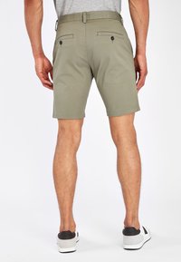 Pantalones cortos cortos en verde oliva con un frente plano, lazos para el cinturón y dos bolsillos traseros con botones. Tela suave y un ajuste entallado.