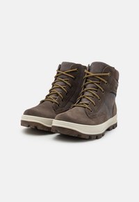 Botas de tobillo de ante marrón con puntera reforzada, costuras en contraste, suela de goma beige y ojales metálicos para los cordones.