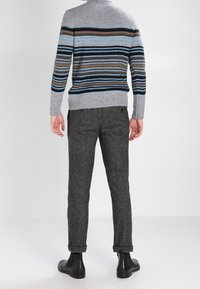 Šedý pruhovaný svetr s modrými, hnědými a černými akcenty, kombinovaný s tmavě šedými kalhotami. Viditelná hladká textura a zúžený střih.