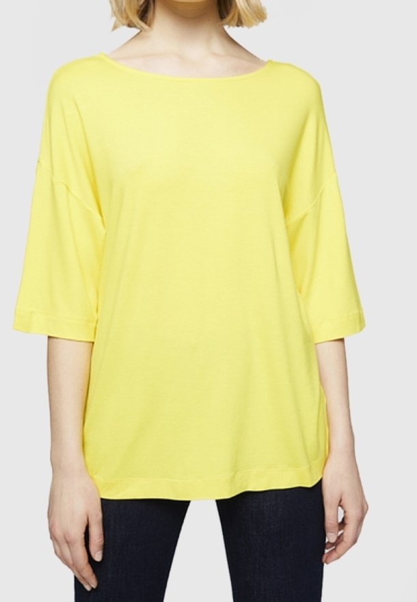 Žluté, oversize, krátké tričko z měkké tkaniny s širokým výstřihem a uvolněným střihem. V kombinaci s tmavými džíny pro kontrast.