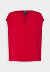 Haut rouge à manches courtes avec un col en V. Texture lisse avec une coupe décontractée et un léger éclat. Étiquette avec le nom de la marque située au niveau du col.