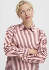 Camicia a righe in morbido tessuto, con linee verticali in tonalità di rosa chiaro e rosa scuro, chiusura frontale con bottoni e colletto classico con maniche lunghe.