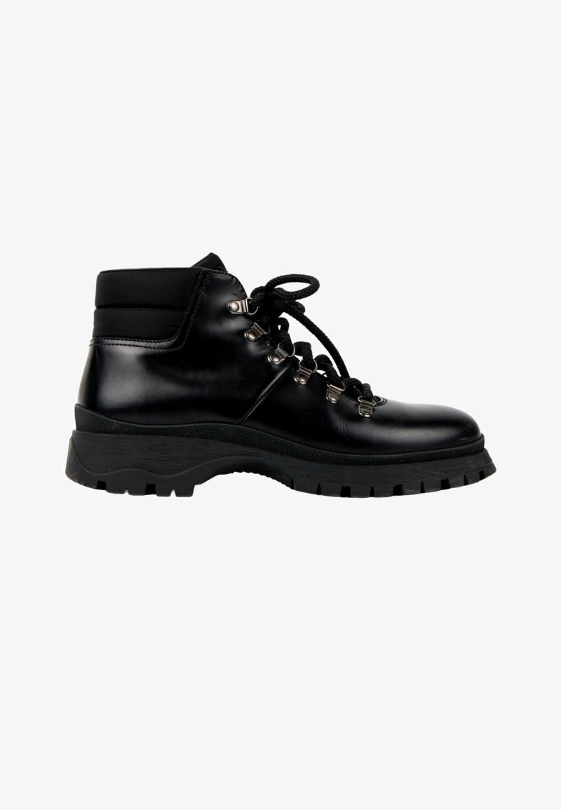 Botte de randonnée en cuir noir à la cheville avec semelle épaisse à crampons, œillets métalliques et lacets noirs sur fond blanc.