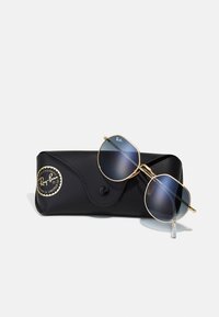 Gafas Ray-Ban con montura de metal dorado y lentes oscuros, reposando sobre un estuche de cuero negro con un logo circular.