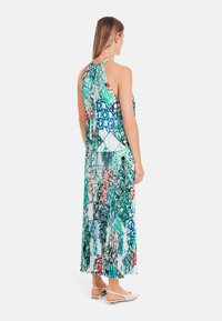 Maxi dress with a halter neck, featuring a colorful patchwork of floral and geometric patterns in green, blue, red, and white. Pleated texture.