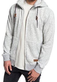 Jasnoszara rozpinana bluza z kapturem wykonana z fakturowanej tkaniny, z sznurkiem w kapturze, kieszeniami z przodu i skórzanym akcentem na dolnym brzegu.