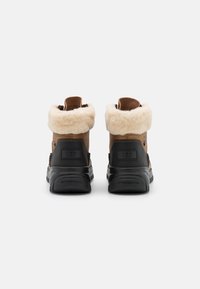 Botas de ante marrón y goma negra hasta el tobillo con forro de piel y cuello acolchado, que cuentan con una suela texturizada y detalle del logo en el talón.