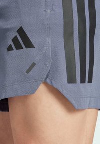 Pantaloni corti sportivi viola realizzati in tessuto testurizzato con il logo Adidas nero e tre strisce verticali nere sul lato.
