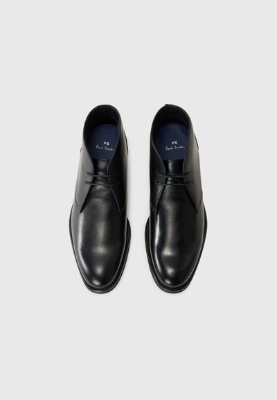 Bottines en cuir noir avec une finition lisse, bouts ronds et un laçage minimal. Elles présentent une semelle intérieure bleu marine avec un détail de logo.