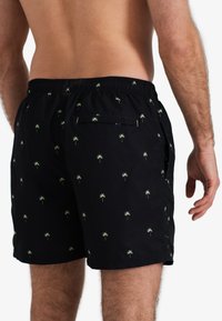 Zwarte zwembroek met een groen palmbomenpatroon, elastische tailleband en een achterzak. Gemaakt van lichte, ademende stof.