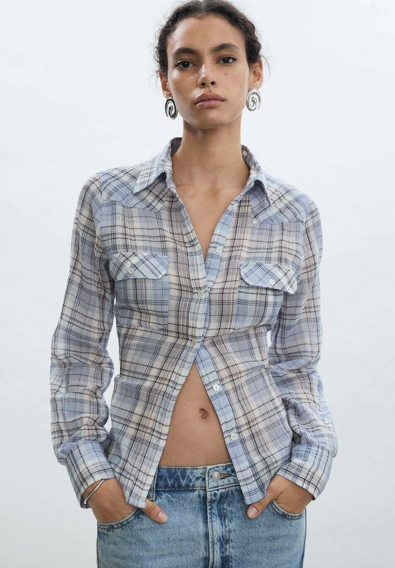 Blue and white plaid shirt with long sleeves, two chest pockets, and a button-down front; paired with high-waisted denim shorts.
