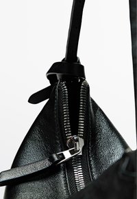 Black leather bag featuring a silver zipper and strap, with a textured finish and a triangular shape. Close-up of hardware detail.
