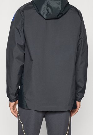 Zwarte hoodie met elastische manchetten gedragen door een persoon die van achteren wordt getoond, gecombineerd met donkere broek met lichte zijstrepen.