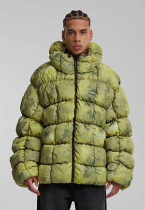 Veste matelassée tie-dye verte avec capuche, fermeture éclair et sections gonflées. Elle possède des poignets élastiques et un petit patch logo sur la poitrine.