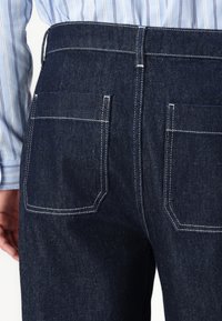 Mörkblå denimjeans med rak passform, med två bakfickor, vit sömnad och en slät yta.