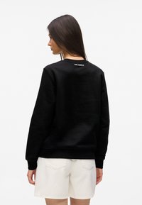 Hanorac negru cu gât rotund dintr-o țesătură moale, cu manșete și tiv striate, având un logo pe spatele gâtului, asortat cu pantaloni scurți albi.