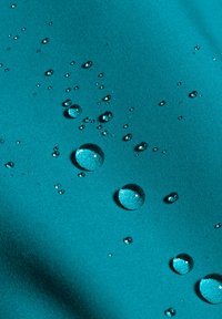 Türkisfarbener Stoff mit glatter Oberfläche, auf dem mehrere Wassertropfen unterschiedlicher Größe liegen und das Licht reflektieren.