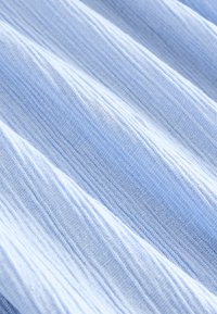 Tissu bleu clair avec un tissage texturé, présentant des rayures horizontales et une apparence légèrement froissée. Texture douce et aérienne.