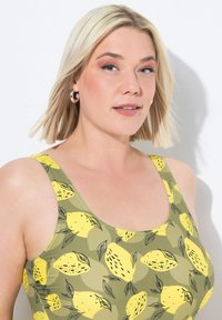 Costume da bagno verde e giallo con motivo a limoni, ampie spalline e una texture del tessuto liscia e elastica.