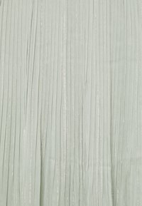 Jupe plissée en tissu vert clair avec des plis verticaux et des accents de fil argenté, créant un effet texturé et scintillant.