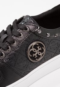 Sneaker in pelle nera con motivo embossato, lacci neri, occhielli in metallo, dettagli in rivetti argentati e distintivo rotondo argentato sulla suola bianca.