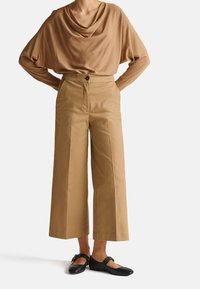 Beżowa bluzka z kołnierzem typu cowl, wysokiej talii be żowe szerokie spodnie oraz czarne baleriny z paskiem na śródstopiu. Czyste linie i miękkie tekstury.