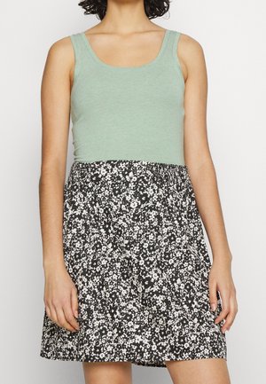 Mátově zelený tílko ve spojení s černou sukní s květinovým vzorem v bílé a krémové barvě. Střih je na horní části přiléhavý a dole se rozšiřuje.