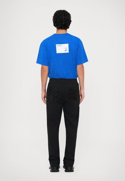 Blue cotton t-shirt with a square graphic on the back, paired with black sweatpants featuring textured black fabric pocket accents.