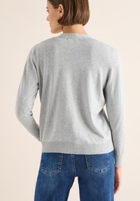 Maglione grigio chiaro a maglia con scollatura rotonda, maniche lunghe e orlo a coste, indossato con jeans blu, che mostrano una texture liscia e uniforme.