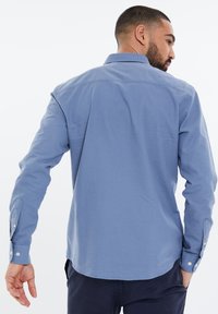 Koszula z długim rękawem w jasnoniebieskim kolorze, z kołnierzykiem zapinanym na guziki i mankietami na jeden guzik. Gładka tekstura, prosty dół.