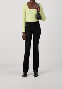 Top de manga larga verde lima con canalé y escote cuadrado, combinado con unos pantalones de campana negros y botines negros, llevando un bolso pequeño.